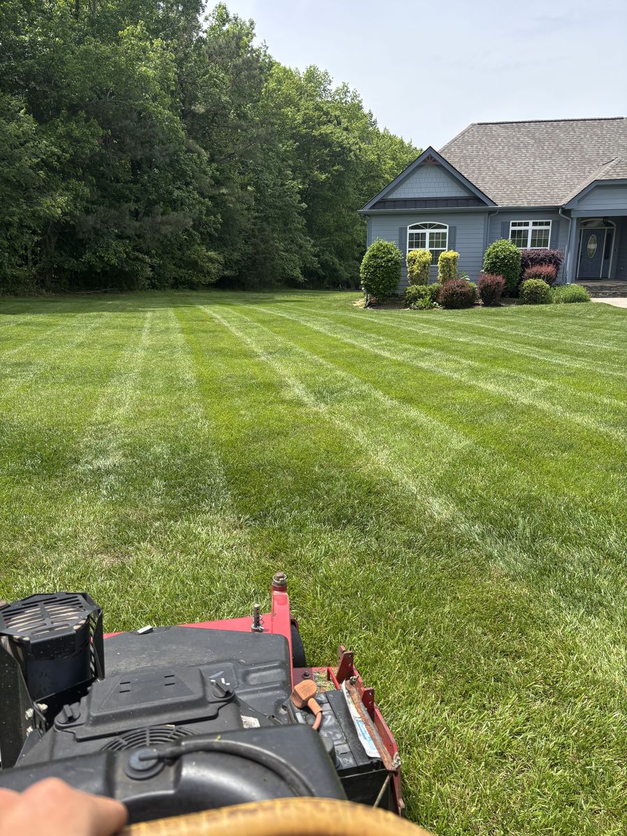 Freshly striped lawn in front of a stone and siding house, mower handle in the foreground
